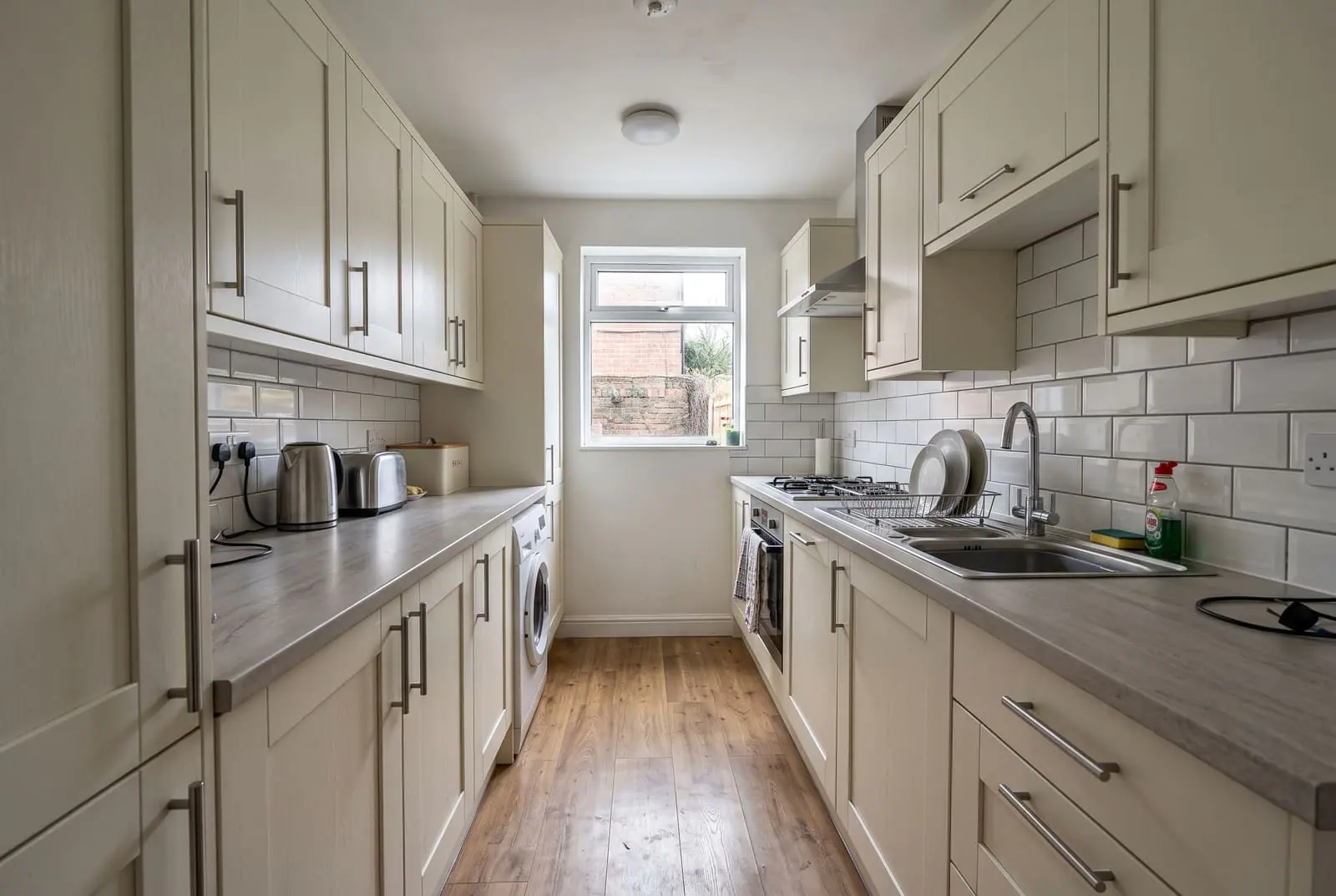 A cream galley kitchen with grey worktops and a window at the end