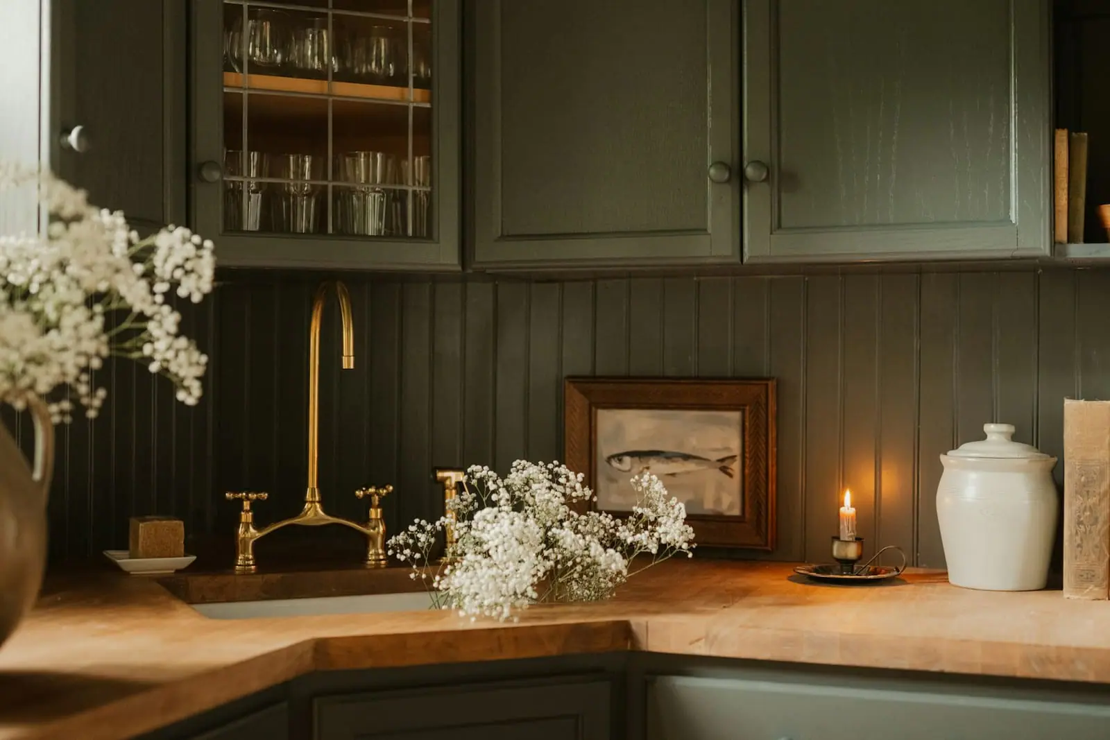 A dark green kitchen with a brass tap and wooden worktop